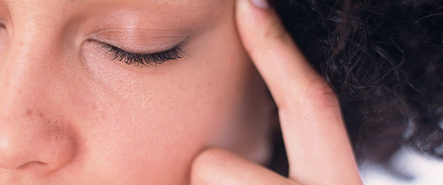 Person experiencing migraine with eyes shut and finger pointing to side of head