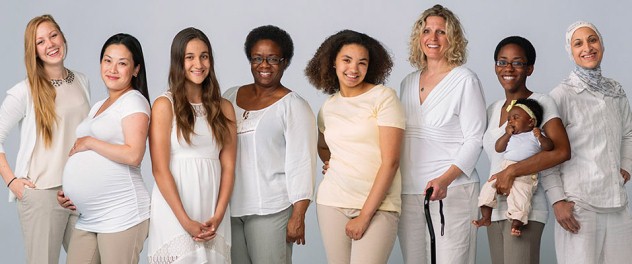 Un gruppo etnicamente diversificato di otto donne di età diverse posa per una foto. Uno è incinta e un altro tiene in braccio un bambino.