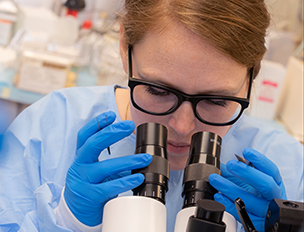 Lab team member examining slide under a microscope.
