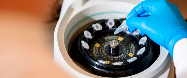 Close up photograph of a person's gloved hand placing a small sample into a microcentrifuge lab device