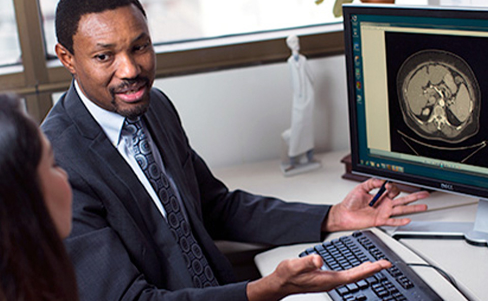 Dr. Lewis Roberts sitting in front of computer monitors discussing imaging with a colleague