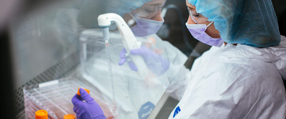 A researcher using a pipette while wearing protective gear.