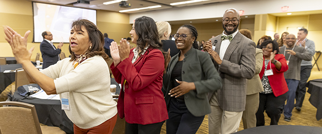 Community Partnership Summit welcome. A line of people are dancing through a conference room.