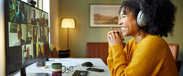 A woman sits in front of a computer screen showing the people on a conference call.