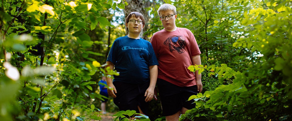 Two teenage boys in forest of green trees